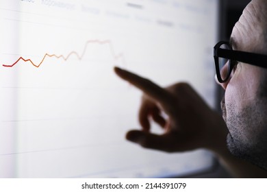 A businessman is looking at a graph on a monitor. An exchange broker evaluates stock market trends. A man with glasses in front of a curve of the dynamics of economy. - Shutterstock ID 2144391079