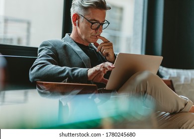 Бизнесмен смотрит на ноутбук и думает. Бизнесмен читает электронные письма на ноутбуке в холле офиса.