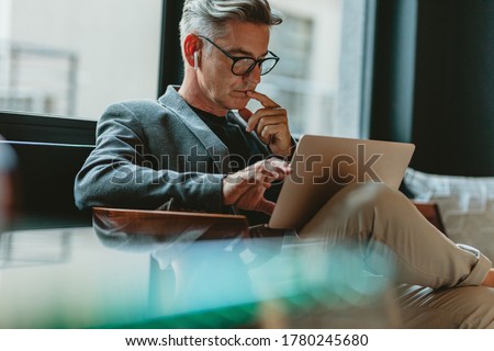 Businessman looking at laptop and thinking. Businessman reading emails on laptop in office lobby.