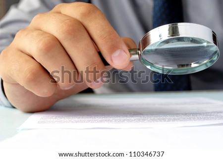 Businessman looking through a magnifying glass to documents