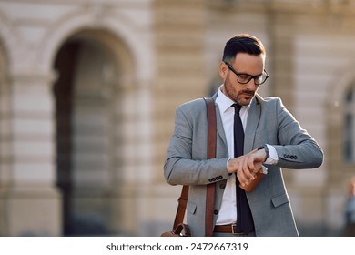 Businessman looking at time on his wristwatch while walking in the city. Copy space. - Powered by Shutterstock