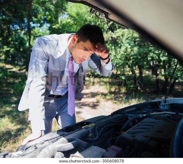 Businessman looking under the hood of breakdown\
car in forest