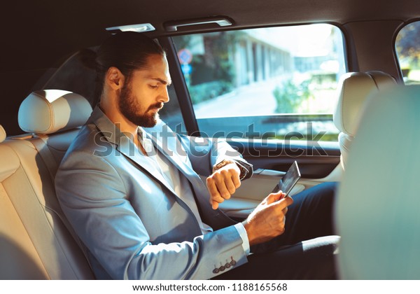 Businessman looking at the watch on the back of\
the limousine