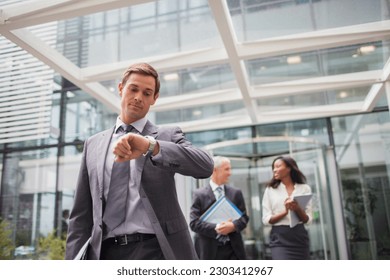 Businessman looking at watch walking out of office building - Powered by Shutterstock