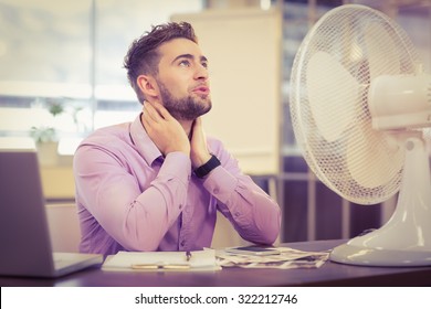 Businessman Looking Up While Sitting At Desk With Electric Fan In Office