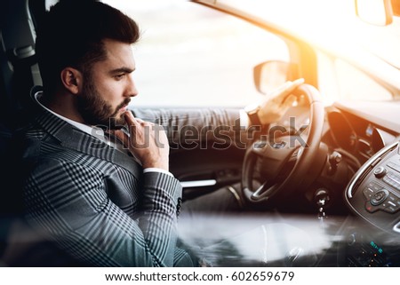 Businessman lost in thought with right hand on chin and left on hand wheel