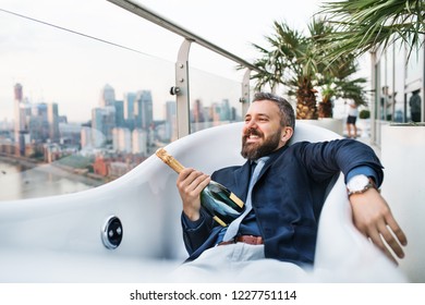 Businessman Lying In Empty Hot Tub, London View Panorama In The Background.