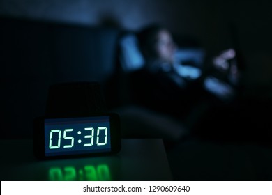 Businessman Lying On The Bed Early In The Morning And Using Tablet. Clock Showing 5:30. Selective Focus On Clock.