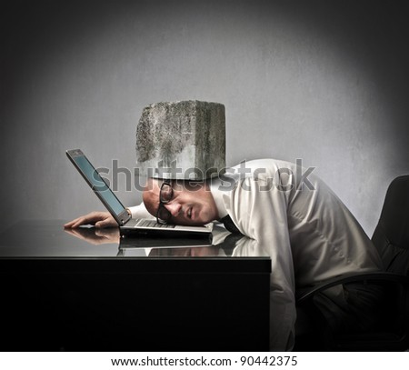 Businessman lying on a laptop with a rock squeezing his head against the laptop keyboard
