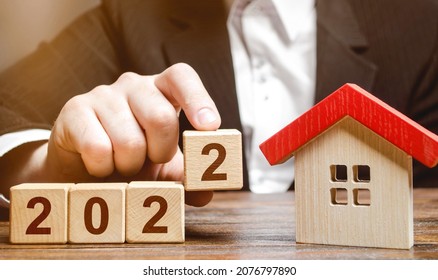 A businessman making 2022 out of blocks near house. Concept of the real estate market in the new year. Forecast of prices and offers, new trends and tendencies. Investment plans. Mortgage loan. - Shutterstock ID 2076797890