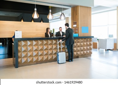 Businessman making booking at front desk with Latin receptionists in hotel lobby 