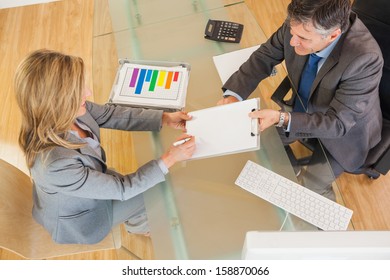 A businessman making a businesswoman signing a contract in an office above a desk