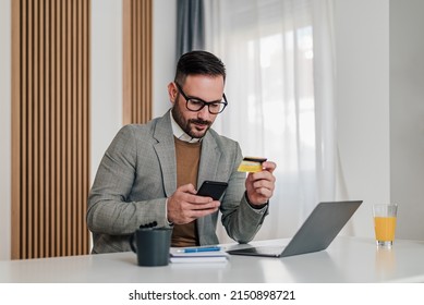 Businessman making card payment through smart phone. Serious Male professional using laptop at desk. He is wearing formals in office. - Powered by Shutterstock