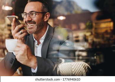 Businessman making a phone call from a coffee shop. Business professional having coffee and talking on speaker phone. - Powered by Shutterstock