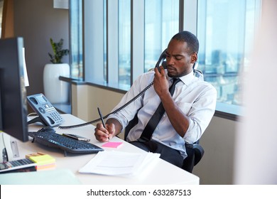 Businessman Making Phone Call Sitting At Desk In Office