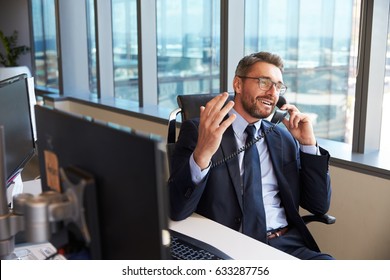 Businessman Making Phone Call Sitting At Desk In Office