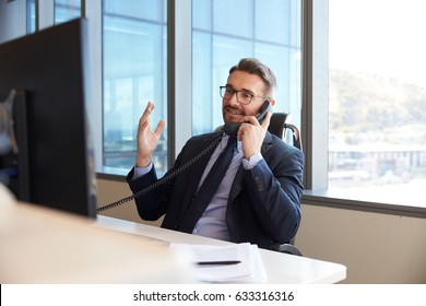 Businessman Making Phone Call Sitting At Desk In Office