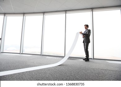 Businessman Or Male Lawyer Unrolling And Reading Long Paper List In Office