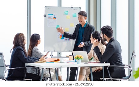 Businessman manager presenter in formal suit standing holding pen pointing at graph chart document on whiteboard presenting company information to Asian male female colleagues in meeting room. - Powered by Shutterstock