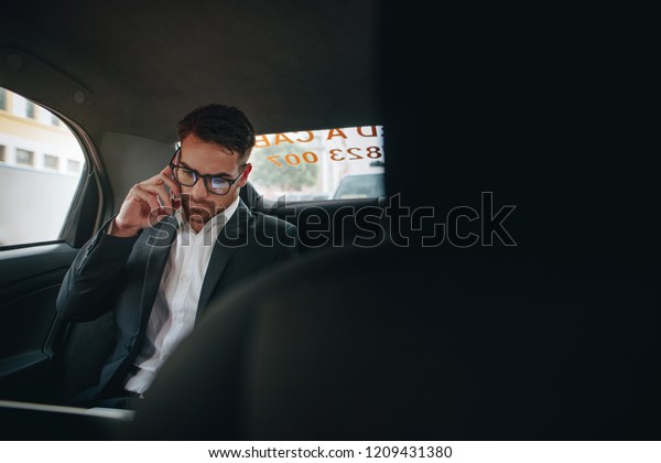 Businessman managing office work on\
the move sitting in a cab. Entrepreneur talking over cell phone and\
looking at office files while commuting to office in a\
taxi.