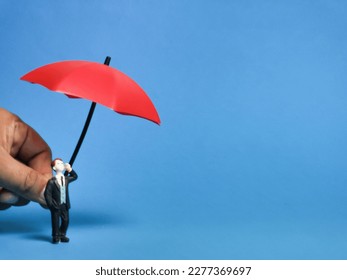 Businessman miniature with hand holding red umbrella.