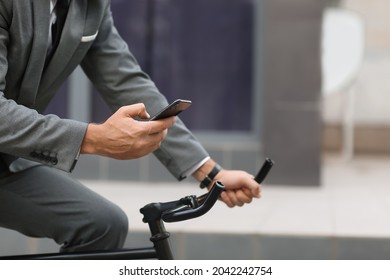 Businessman With Mobile Phone Riding Bicycle On City Street