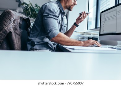 Businessman with mobile phone sitting in office and working on computer. Young businessman talking on mobile phone and using computer in office. - Shutterstock ID 790755037