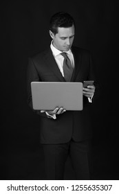 Businessman. Mobile Phone While Working On Laptop On Black Background. Man Or Manager Wearing Formal Blue Suit. Technology For Business. Messaging. Fashion And Dress Code