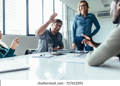 Businessman offering a high five to a coworker during a meeting in conference room. Positive boardroom environment. - Powered by Shutterstock