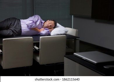 A businessman in office clothes comfortably sleeping on a conference table with a pillow