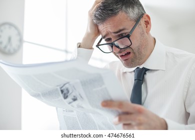 Businessman In The Office, Reading Bad Breaking News On A Business Newspaper, He Is In Panic And Touching His Head, Financial Crisis Concept