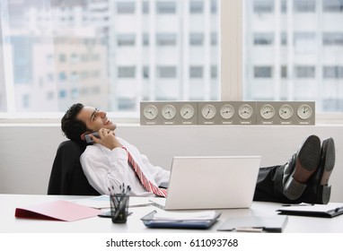 Businessman in office, using mobile phone, feet up on desk