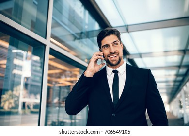 Businessman On Business Trip Talking On His Mobile Phone At Airport. Caucasian Businessman Using Mobile Phone And Smiling.