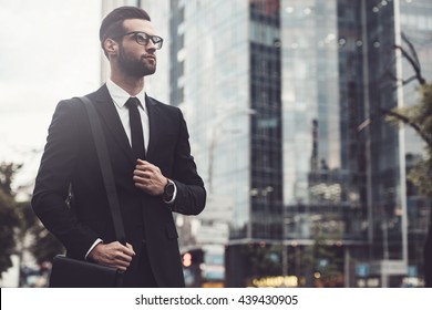 Businessman On The Go. Low Angle View Of Confident Young And Handsome Man In Full Suit Walking Along The Street With Cityscape In The Background