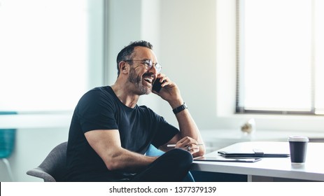 Businessman on mobile phone while working at office. Man sitting at his desk talking on mobile phone and laughing. - Powered by Shutterstock