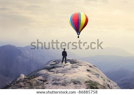 Businessman on a peak observing a hot-air balloon