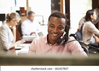 Businessman On Phone At Desk With Meeting In Background - Powered by Shutterstock