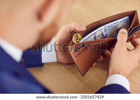 Businessman opens wallet with money. Closeup man's hands on wooden table holding leather wallet with paper USD banknotes and golden bitcoin symbol. Business, finance, currency, cryptocurrency concept