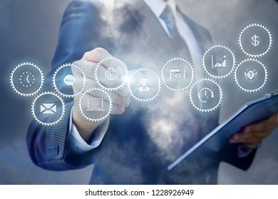 A Businessman Is Operating With The Cogwheel Mechanism Containing Icons And Symbols While Making Notes. The Concept Is The Optimization Of The Existing Business System.