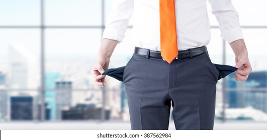 A Businessman With An Orange Tie Turning His Empty Pockets Inside Out. Front View, No Head. Blurred Office At The Background. Concept Of Bankruptcy.