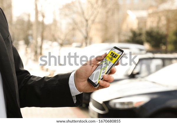 Businessman ordering taxi with smartphone on city\
street, closeup