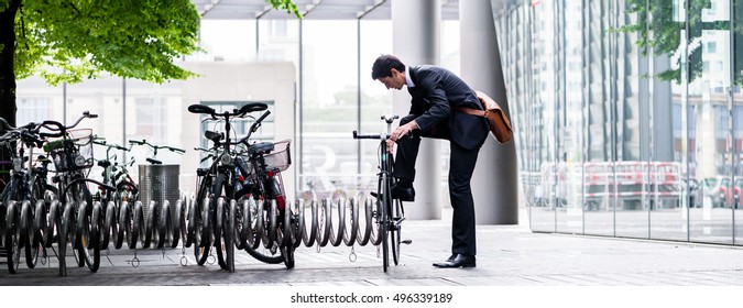 Businessman parking his bicycle in town at bicycle rack after commuting to work in concept eco  friendly transport   healthy active lifestyle  panoramic banner view