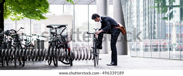 Businessman parking his\
bicycle in town at a bicycle rack after commuting to work in a\
concept of eco-friendly transport and healthy active lifestyle,\
panoramic banner\
view