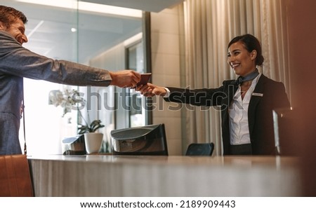 Businessman passes his passport to a smiling receptionist behind the hotel counter. Check-in process in luxurious hotel.