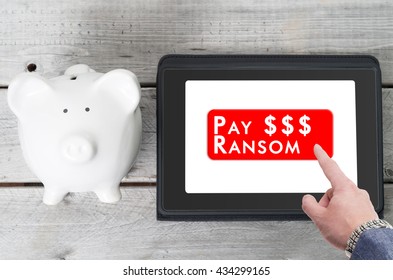 Businessman Paying A Ransom To Ransomware On A Tablet Device With Piggy Bank Next To It