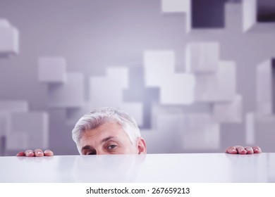 Businessman Peeking Over Desk Against Abstract White Room