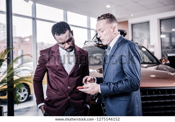 Businessman with\
phone. Businessman wearing dark suit holding his phone while asking\
some questions about new\
car