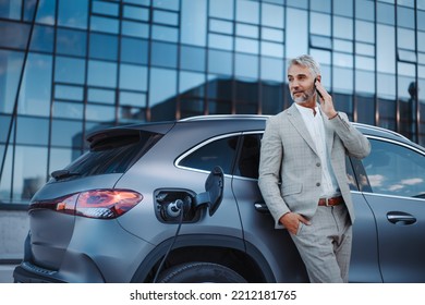 Businessman phoneing while charging car at electric vehicle charging station, closeup. - Powered by Shutterstock