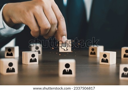  Businessman picked up a wooden block with an Ai icon, surrounded by wooden blocks with a human icon. AI vs human competition.the impact of artificial intelligence and robotics on Unemployment.