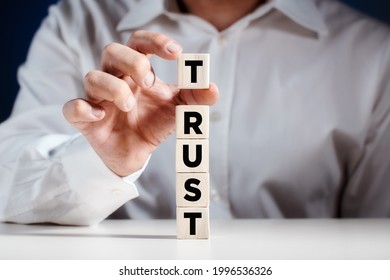 Businessman Placing Cube On Top Of Tiered Wooden Cubes And Completing The Word Trust. Building Trust In Business Concept.
